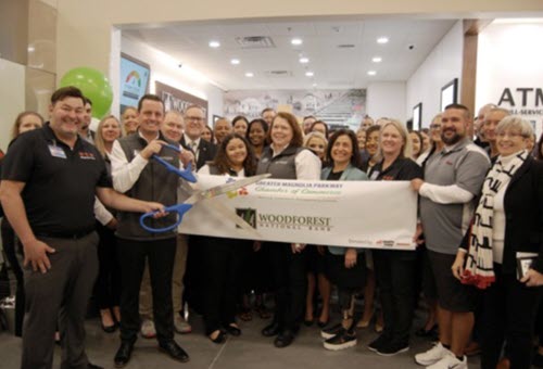 Officiating the ribbon cutting ceremony are Woodforest’s Brett Simms, Assistant VP and Branch Manager (holding scissors) and Julie Mayrant, President and Chief Retail Officer (4th from right, front row), with H-E-B store manager John Beardsley (far left) and Sandy Barton, President of the Greater Magnolia Parkway Chamber of Commerce (far right).