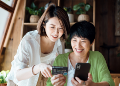 Dos mujeres observando un teléfono móvil y una tarjeta de débito